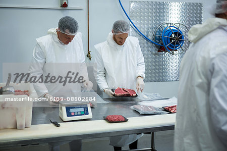 Butchers weighing packages of meat at meat factory