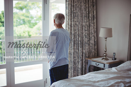 Senior man looking through window in bedroom at home