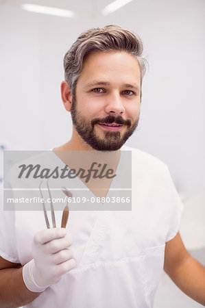 Dentist holding dental tweezers and mouth mirror in clinic