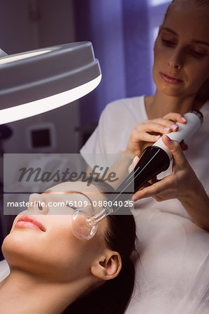 Dermatologist performing laser hair removal on patient face in clinic