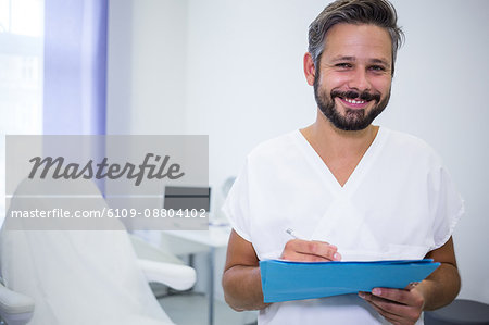 Portrait of smiling doctor writing on medical reports in clinic