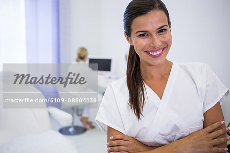 Portrait of smiling dentist standing with arms crossed at clinic