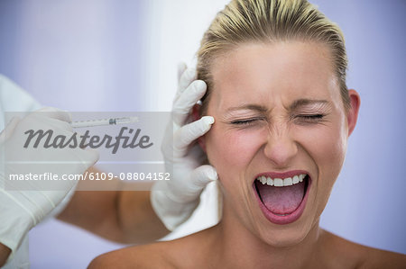 Close-up of scared woman shouting while receiving an injection from cosmetic treatment