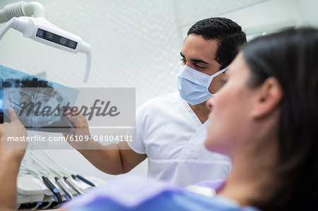 Young male dentist examining X-ray with the female patient at the clinic