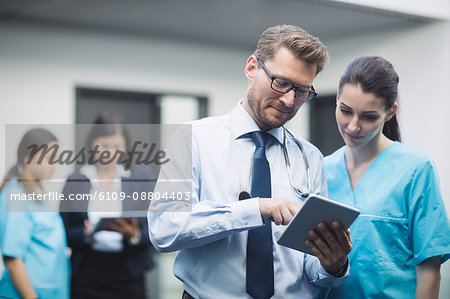 Doctor and nurse discussing over digital tablet in hospital corridor