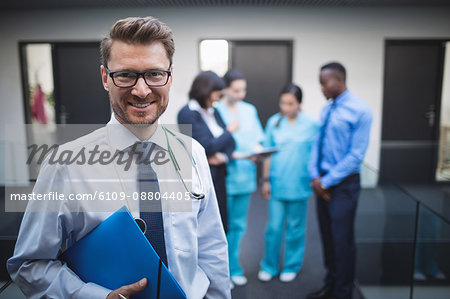 Portrait of smiling doctor holding medical report in hospital corridor