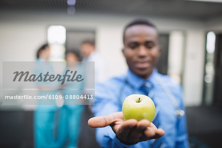 Close-up of doctor showing green apple in hospital corridor