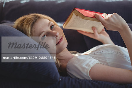 Portrait of beautiful woman lying on sofa and reading book in living room at home