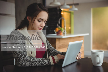Woman using digital tablet while having coffee at home