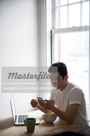 Man using mobile phone while having breakfast at home