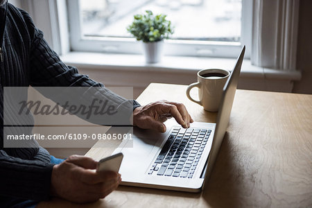 Mid-section of man using laptop and mobile phone at home