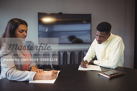 Businesswoman and colleague writing in a diary in conference room at office