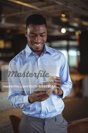 Businessman holding disposable coffee cup and using mobile phone in office