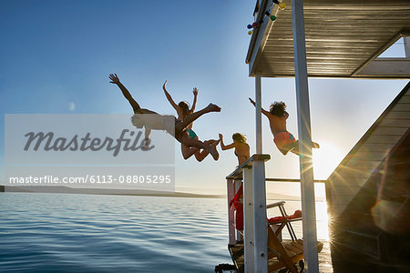 Young adult friends jumping from summer houseboat into sunny ocean