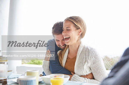 Affectionate couple hugging and laughing at breakfast on patio