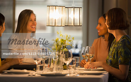 Smiling women friends dining and drinking wine at restaurant table