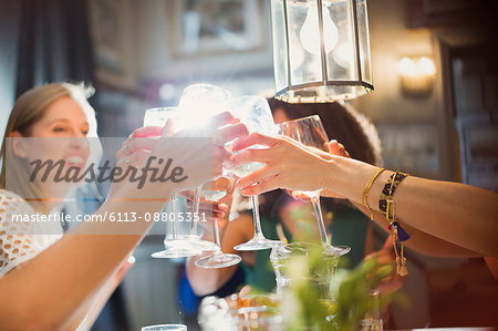 Smiling women friends toasting wine glasses dining at restaurant table