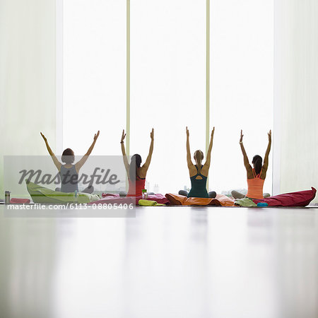 Women on cushions with arms raised in restorative yoga gym studio