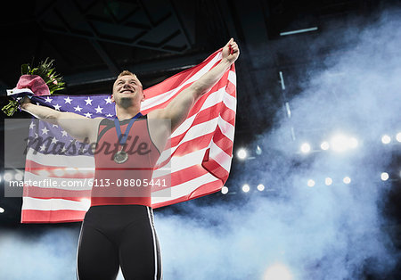 Male gymnast celebrating victory holding American flag on winners podium