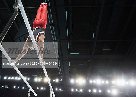 Male gymnast performing upside-down handstand on parallel bars in arena