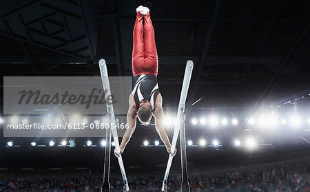 Male gymnast performing upside-down handstand on parallel bars in arena