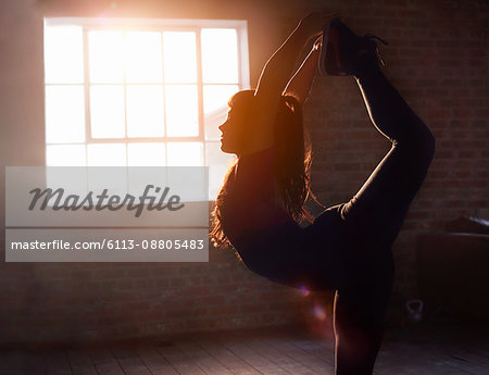 Silhouette female dancer stretching practicing yoga king dancer pose in studio