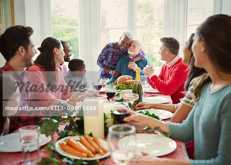 Affectionate multi-ethnic senior couple hugging at family Christmas dinner table