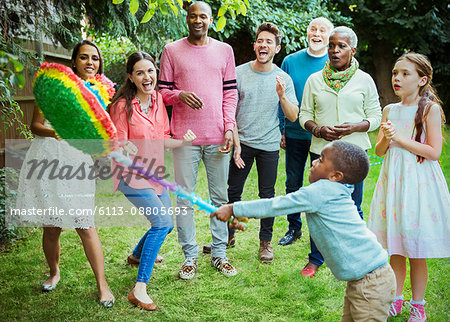 Multi-ethnic multi-generation family cheering boy hitting pinata at birthday party