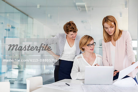 Female architects at laptop reviewing blueprints in conference room meeting
