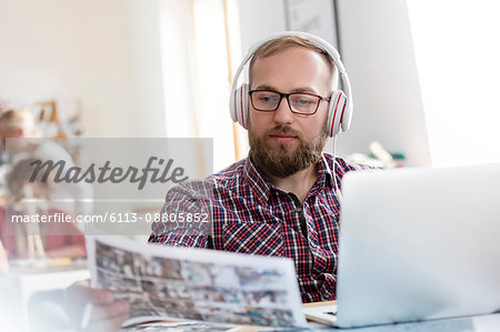 Design professional listening to music with headphones reviewing proofs at laptop