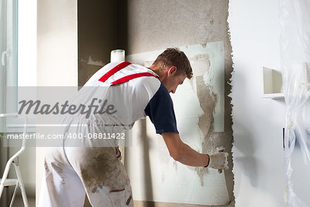 Thirty years old manual worker with wall plastering tools renovating house. Plasterer renovating indoor walls and ceilings with float and plaster.