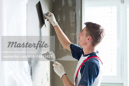 Thirty years old manual worker with wall plastering tools renovating house. Plasterer renovating indoor walls and ceilings with float and plaster.