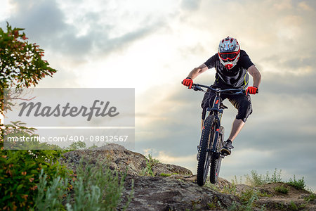 Professional Cyclist Riding the Bike Down Rocky Hill at Sunset. Extreme Sport Concept. Space for Text.