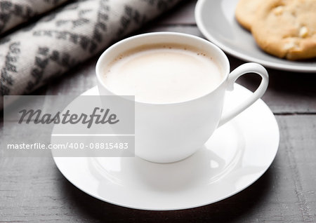 Cup of cappuccino with grey wool scarf and cookies on wooden background