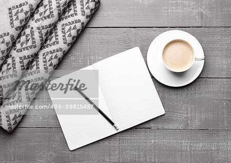 Cup of cappuccino with grey wool scarf and diary book on wooden background
