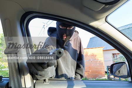 An armed man in the mask threatening pistol to the driver of the car