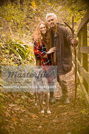 Portrait smiling couple with dog and walking stick along autumn fence