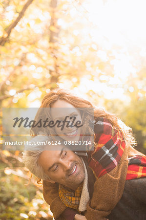 Portrait playful couple piggybacking in autumn woods