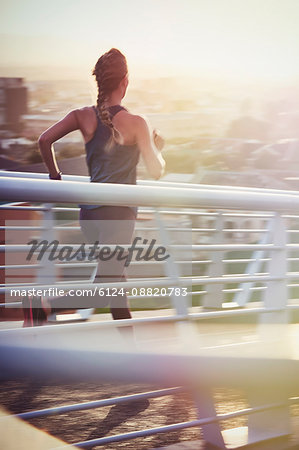 Female runner running on sunny urban footbridge at sunrise