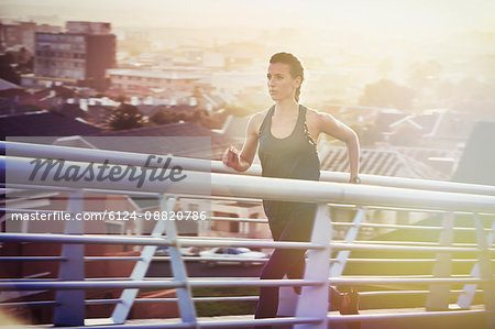 Determined female runner running up urban footbridge at sunrise