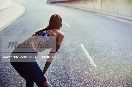 Fit female runner in sports bra with mp3 player arm band resting on urban street
