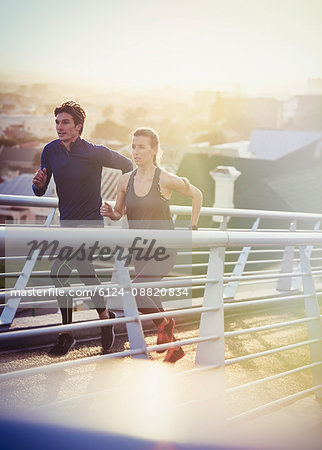Runner couple running on sunny urban footbridge at sunrise