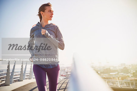 Female runner running on sunny urban footbridge at sunrise