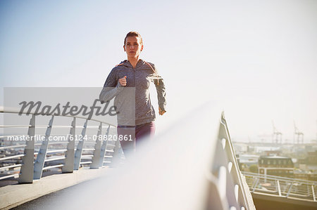 Female runner running on sunny urban footbridge