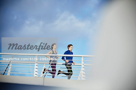 Runner couple running on sunny footbridge