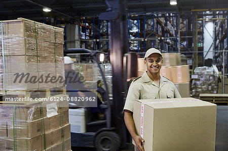 Portrait smiling worker carrying cardboard box at distribution warehouse loading dock