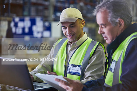 Workers with clipboard and laptop working in distribution warehouse