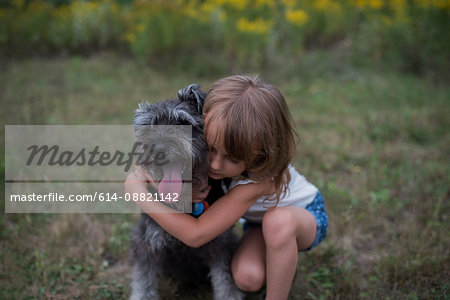 Little girl hugging pet dog on grass field