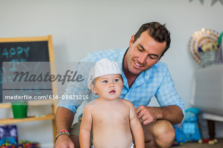 Father smiling at toddler wearing funny hat