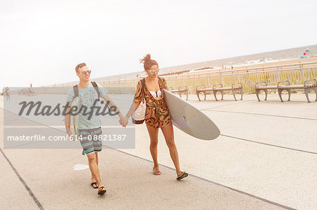 Young couple holding hands and carrying surfboards at Rockaway Beach, New York State, USA